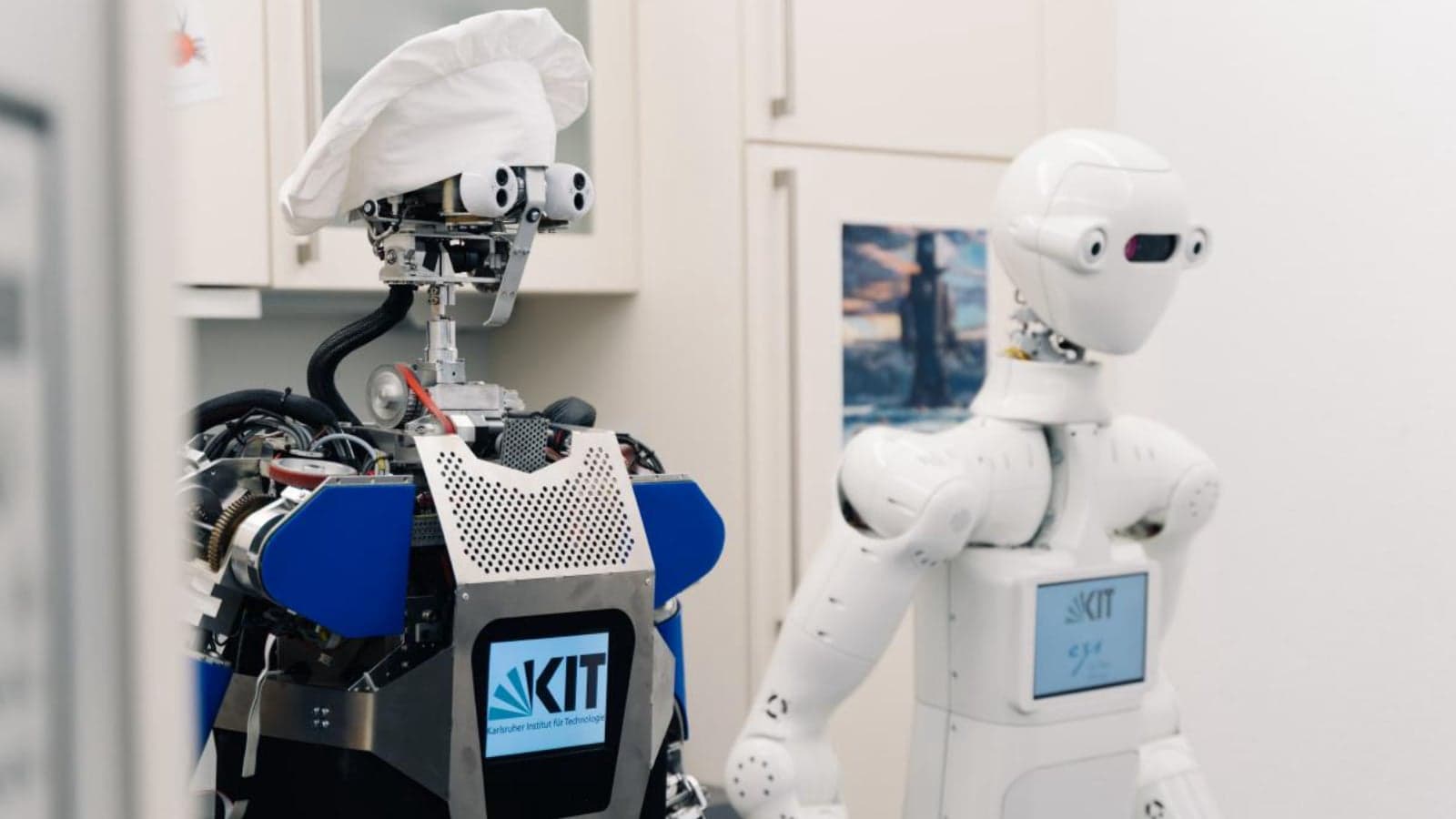 Twee mensachtige onderzoeksrobots in een keuken, een met een koksmuts, als voorbeeld van AI in fysiek werk